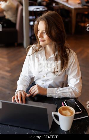 Happy young woman sipping coffee in a cozy café setting. Calm and inspiring atmosphere, concept of remote work, freelancing, or mindful morning routin Stock Photo