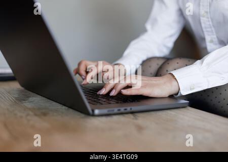 Woman typing on laptop in elegant office outfit. Focus on hands and keyboard, showing concentration, technology, and work-from-home lifestyle. Stock Photo