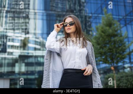 Stylish woman in sunglasses posing confidently in urban environment. Modern business attire and city lifestyle concept. Stock Photo