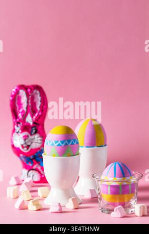 Easter still life with hand painted eggs, chocolate bunny and heart shaped marshmallows on a pink background. Bright holiday composition for spring ce Stock Photo