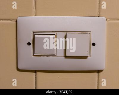 White rectangular electrical panel featuring a light switch and a doorbell button, showing signs of wear and dirt, fixed on a yellow tiled wall in alm Stock Photo