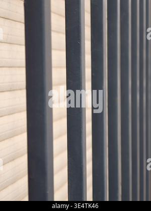 Dark gray metal bars creating a protective barrier and linear pattern against a light colored, horizontally corrugated background, emphasizing concept Stock Photo