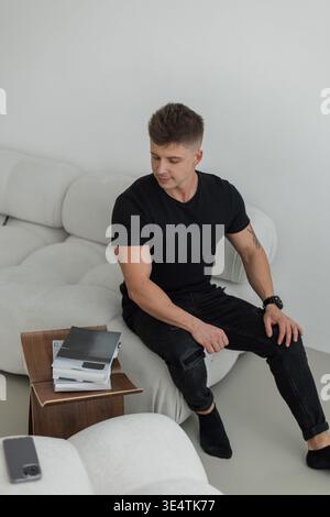 Handsome successful businessman man in black fashion clothes sitting on sofa with magazines at home Stock Photo