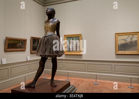 Little Dancer Aged Fourteen by Degas at The Met, NYC. Bronze sculpture with impressionist ballet paintings by Degas visible in background. Stock Photo