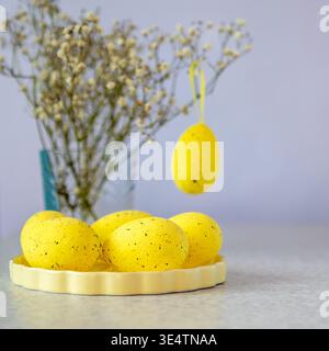 Yellow speckled Easter egg arrangement on plate with hanging egg and delicate spring flowers Stock Photo