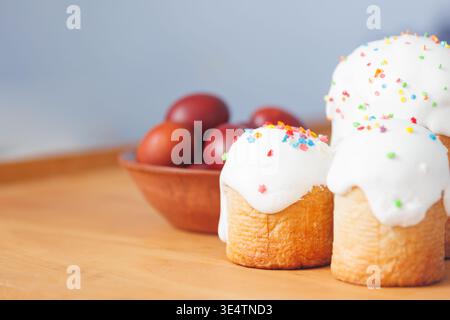 Fresh homemade Easter bread paska with sugar glaze and colorful eggs on wood background, selective focus and copy space. Stock Photo