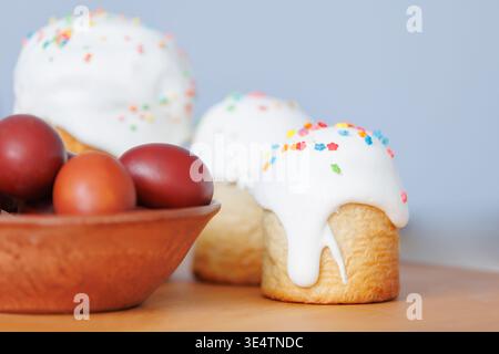 Easter eggs in a brown ceramic bowl with glazed cakes in the background, simple rustic composition on wooden texture. Stock Photo