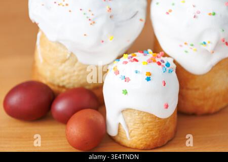 Close-up of small Easter paska cake with white icing and red eggs on a wooden table, traditional festive food details. Stock Photo