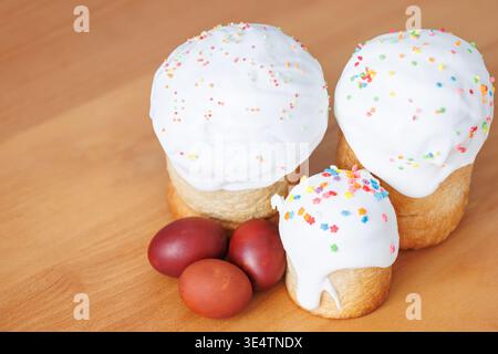 Three Easter cakes with sugar topping and red painted eggs on a natural wood surface, rustic festive background for banner. Stock Photo