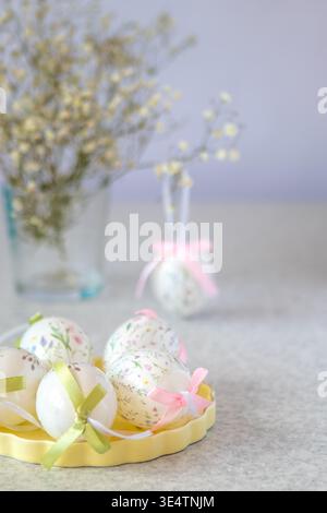 Pastel floral Easter eggs with ribbon bows on a yellow tray and soft spring bouquet Stock Photo