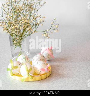 Easter eggs with pastel bows and delicate flowers arranged on a light table for spring decor Stock Photo