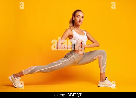 Woman Doing Deep Lunge Exercise Over Yellow Background Stock Photo