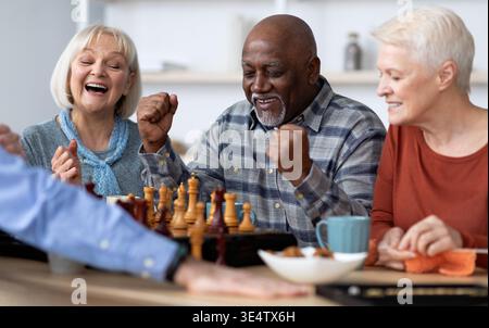 Emotional black man playing chess with multiracial friends Stock Photo