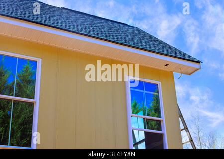 Worker installing yellow primed smooth siding house with tall windows, ladder in place Stock Photo