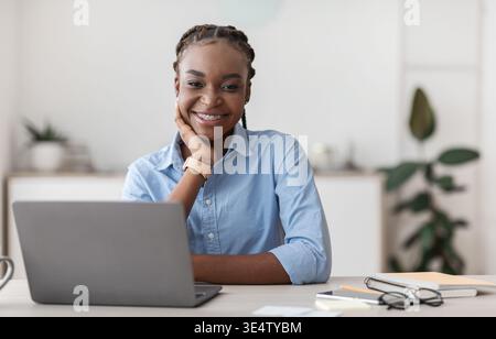 Portrait of young black businesswoman sitting at desk in office Stock Photo