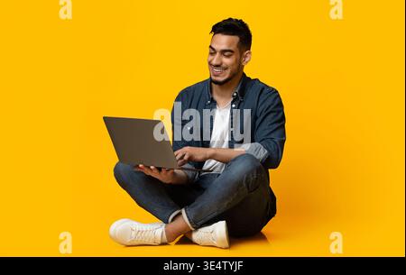 Happy middle eastern guy using modern notebook, isolated on yellow Stock Photo