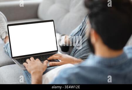 Indian Man Using Laptop Computer With Blank White Screen At Home Stock Photo
