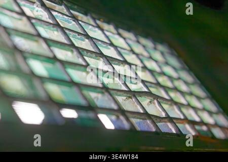 A weathered metal grid with chipped green paint showing rust and wear, illuminated by light shining through the openings in an industrial environment. Stock Photo