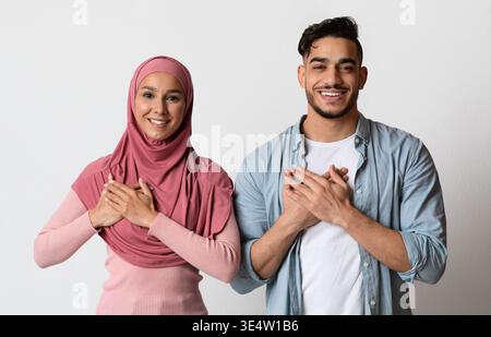 Grateful muslim couple keeping both hands on chest, expressing gratitude and appreciation Stock Photo
