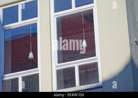 Exterior view of modern building windows showing reflections of hanging lights and ceiling panels with shadows cast on the adjacent wall. Stock Photo