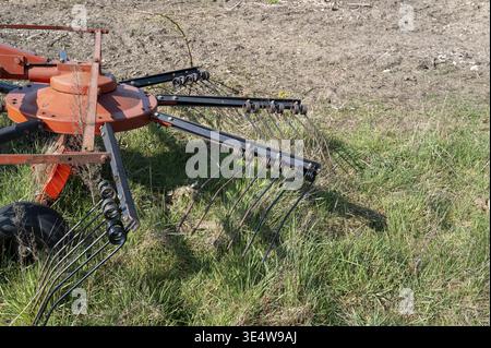 Rotary hay rake tedder agricultural machinery with tines standing on a green farm field Stock Photo
