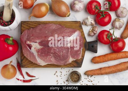 Food, Organic raw pork meat on chopping board and fresh vegetables (tomatoes, onions, garlic, carrots, peppers) on Marble background, spices (coriande Stock Photo
