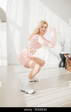 Woman in trendy pink activewear enjoying a workout moment in a sunny home studio. Youthful energy and fitness inspiration. Stock Photo