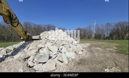 An excavator works on a large pile of rocks on a construction site under clear skies. Recycled reinforced concrete after dismantling a wind turbine fo Stock Photo