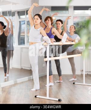 Woman with group of ballet beginners stretching at barre in studio Stock Photo