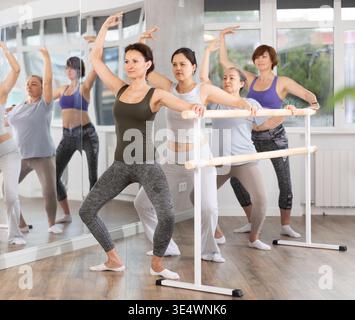 Woman performing demi plie in group barre session in fitness studio Stock Photo