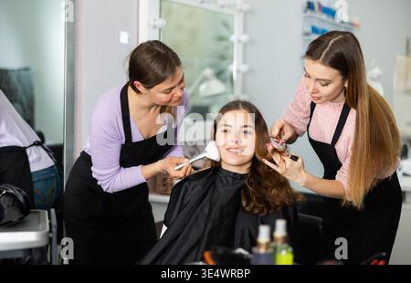 Professional female stylists making hairstyle and makeup to young woman Stock Photo