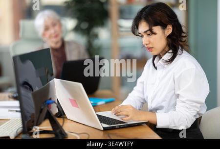 Young woman works on laptop with female colleagues Stock Photo