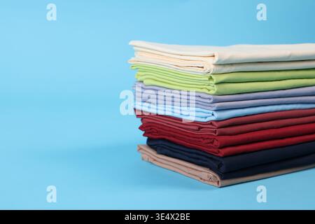 Stack of colorful bed linens on light blue background, closeup. Space for text Stock Photo