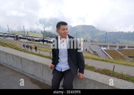 Asian man sitting at the summit of Mount Rigi, Switzerland, looking away Stock Photo
