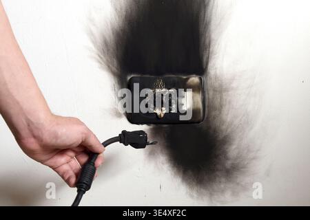 Hand with burnt cable. Isolated electrical fault in the plug. Fire hazard. Stock Photo