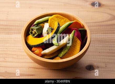 Assorted colorful vegetable chips in a wooden bowl on a rustic wooden table Stock Photo