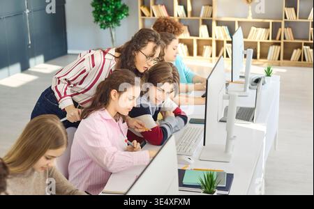 Teacher guiding teen students at computers in classroom lab, collaborative learning Stock Photo