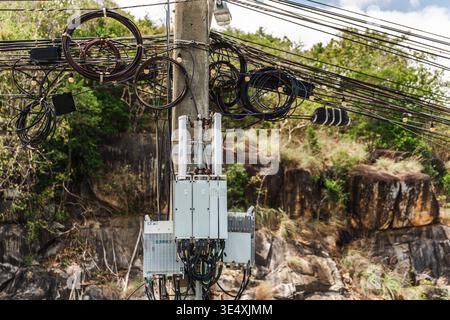 Telecommunication equipment and tangled overhead cables mounted on concrete utility pole in tropical Thailand Stock Photo
