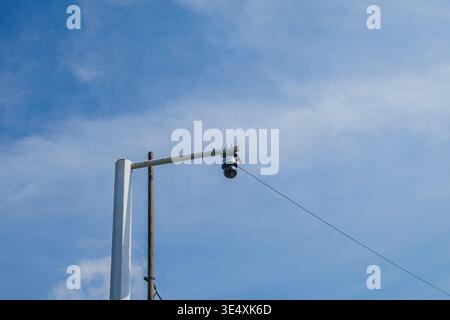 A low-angle shot of a dome-shaped CCTV security camera attached to a white metal pole. Stock Photo
