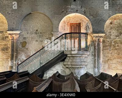A staircase leads up to an illuminated pulpit looking out over the pews of a church in Dinan, France. Stock Photo