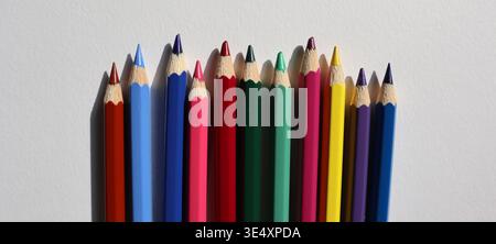 A group of colored pencils is placed in a row on a flat surface. The pencils include various bright colors. This setup is for drawing and creative art Stock Photo