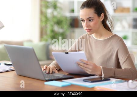 Freelance worker working online holding documents and using laptop in a house interior Stock Photo