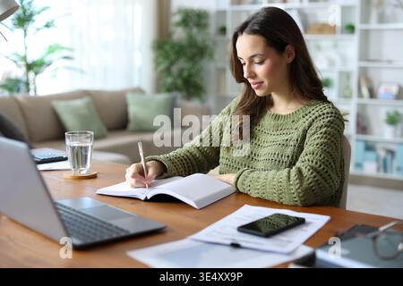 Tele worker writing in paper agenda working at home on a wooden table Stock Photo
