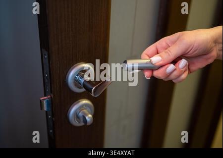 A person holding a detached silver lever from a wooden room door. Close-up of damaged interior hardware needing fix or replacement. Concept of househo Stock Photo