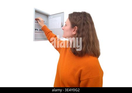Woman electrician checking electrical fuse box at home. Person switching miniature circuit breaker in distribution panel. Repair service, energy safet Stock Photo