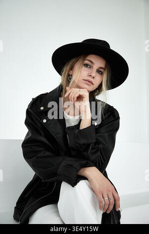 Stylish young woman in black fedora hat and leather jacket looking at camera, portrait. Stock Photo