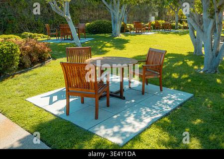 Alfresco Dining Setup. Sunlit Patio With Wooden Furniture. Serene Backyard Scene With Outdoor Table And Chairs Stock Photo