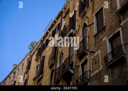 A charming view of traditional Venetian buildings featuring ornate balconies and shutters set against a vibrant blue sky, evoking a sense of timeless Stock Photo