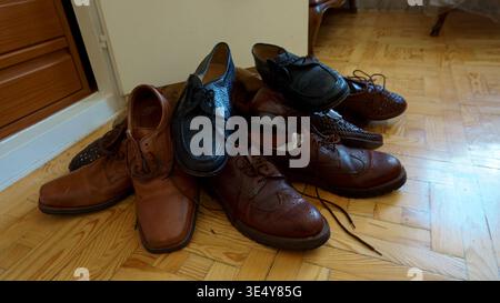 Collection of various brown and black men's leather shoes untidily placed on a wooden parquet floor Stock Photo