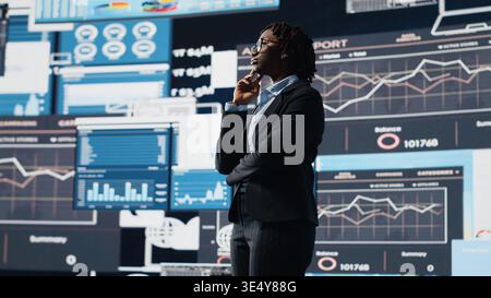 Business manager looking at graphs on digital screens, thinking how to increase company profits. African american woman reading KPI metrics projected on digital screen during decision making, camera B Stock Photo